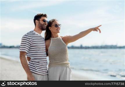 summer holidays and people concept - happy couple pointing finger on beach. happy couple pointing finger on summer beach