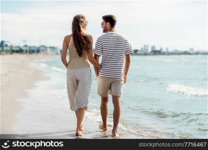 summer holidays and people concept - happy couple walking along beach in tallinn, estonia. happy couple walking along summer beach