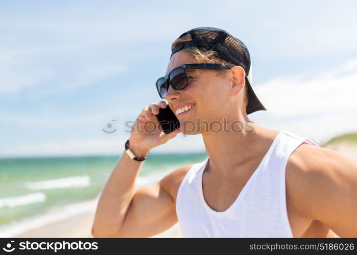 summer holidays and people concept - happy smiling young man in sunglasses calling on smartphone on beach. smiling man calling on smartphone on summer beach