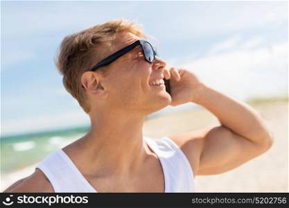 summer holidays and people concept - happy smiling young man in sunglasses calling on smartphone on beach. smiling man calling on smartphone on summer beach