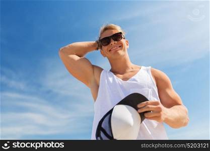 summer holidays and people concept - happy smiling young man in sunglasses with hat over blue sky. smiling young man in sunglasses over blue sky
