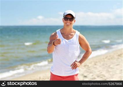 summer holidays and people concept - happy smiling young man in sunglasses and cap on beach showing thumbs up gesture. smiling man on summer beach showing thumbs up
