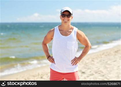 summer holidays and people concept - happy smiling young man in sunglasses and cap on beach. smiling young man in sunglasses on summer beach