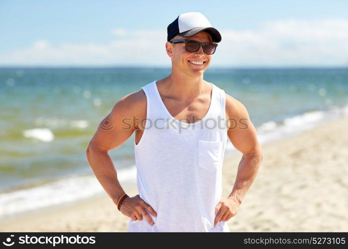 summer holidays and people concept - happy smiling young man in sunglasses and cap on beach. smiling young man in sunglasses on summer beach