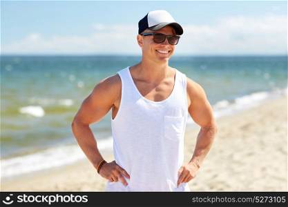 summer holidays and people concept - happy smiling young man in sunglasses and cap on beach. smiling young man in sunglasses on summer beach