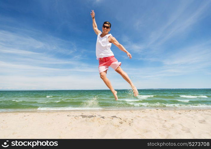 summer holidays and people concept - happy smiling young man jumping on beach. smiling young man jumping on summer beach