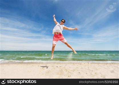 summer holidays and people concept - happy smiling young man jumping on beach. smiling young man jumping on summer beach