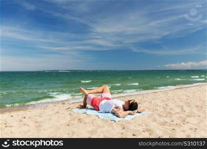 summer holidays and people concept - happy smiling young man sunbathing on beach towel. happy smiling young man sunbathing on beach towel