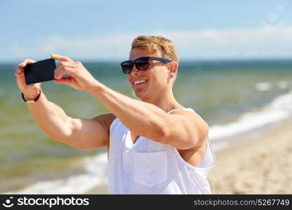 summer holidays and people concept - happy smiling young man taking selfie by smartphone on beach. man taking selfie by smartphone on summer beach