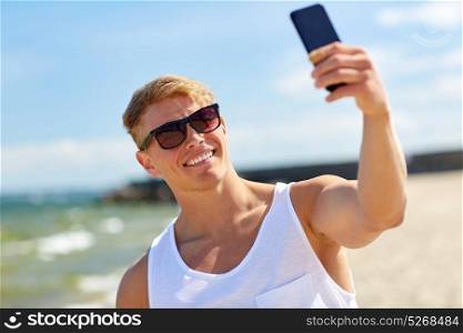 summer holidays and people concept - happy smiling young man taking selfie by smartphone on beach. man taking selfie by smartphone on summer beach