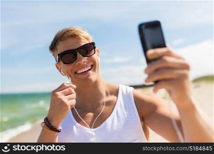 summer holidays and people concept - happy smiling young man with earphones and smartphone taking selfie on beach. man with smartphone taking selfie on summer beach