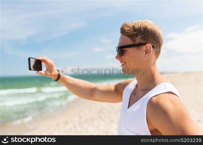 summer holidays and people concept - happy smiling young man with smartphone on beach photographing sea. man with smartphone photographing on summer beach