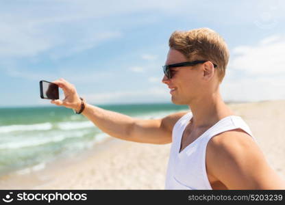 summer holidays and people concept - happy smiling young man with smartphone on beach photographing sea. man with smartphone photographing on summer beach