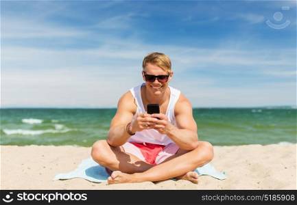 summer holidays and people concept - happy smiling young man with smartphone sunbathing on beach towel. happy smiling young man with smartphone on beach