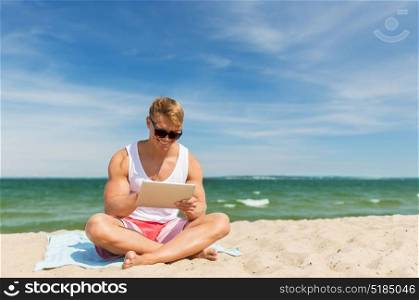 summer holidays and people concept - happy smiling young man with tablet pc computer sunbathing on beach towel. happy smiling young man with tablet pc on beach