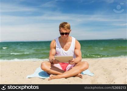 summer holidays and people concept - happy smiling young man with tablet pc computer sunbathing on beach towel. happy smiling young man with tablet pc on beach