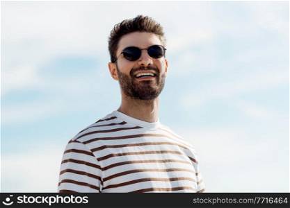 summer holidays and people concept - portrait of happy smiling young man in sunglasses over sky. smiling young man in sunglasses over sky