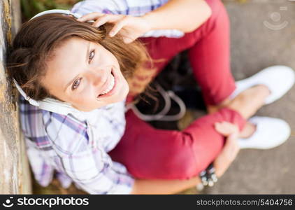 summer holidays and technology concept - teenage girl with headphones listening to music outside