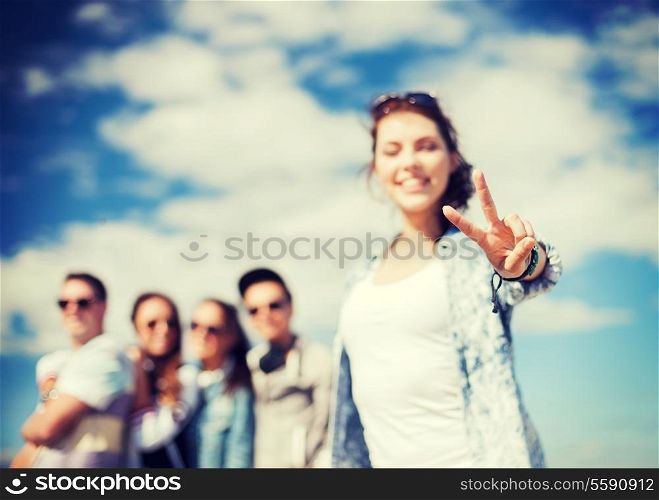 summer holidays and teenage concept - close up of female hand showing v-sign with fingers with friends on the back