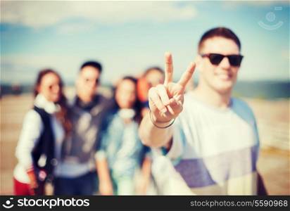 summer holidays and teenage concept - close up of male hand showing v-sign with fingers with friends on the back