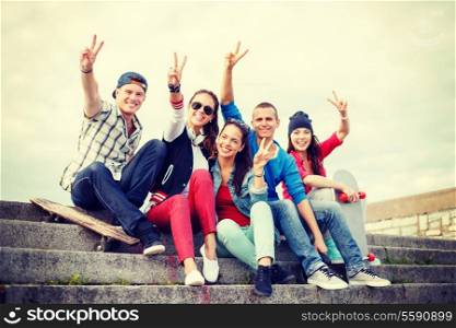 summer holidays and teenage concept - group of smiling teenagers hanging outside and showing v-sing