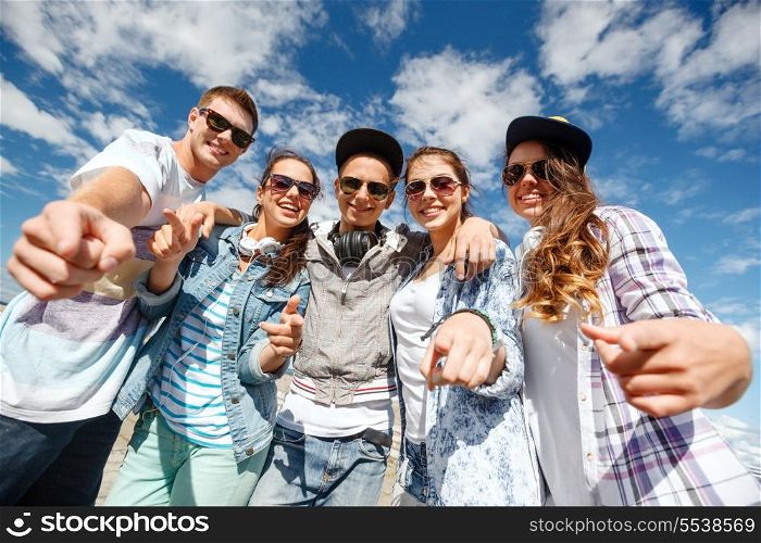 summer holidays and teenage concept - group of smiling teenagers in sunglasses hanging outside pointing finger at you