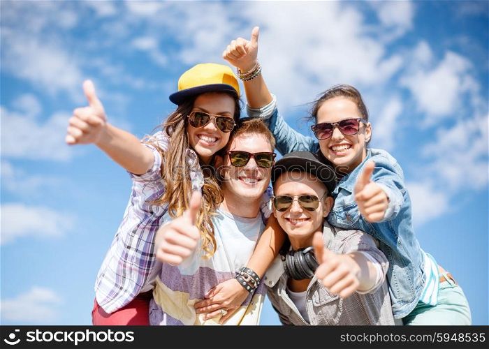 summer holidays and teenage concept - group of smiling teenagers in sunglasses hanging outside and showing thumbs up. smiling teenagers in sunglasses hanging outside