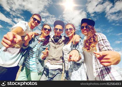 summer holidays and teenage concept - group of smiling teenagers in sunglasses hanging outside pointing finger at you. smiling teenagers in sunglasses hanging outside