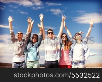 summer holidays and teenage concept - group of smiling teenagers in sunglasses holding hands up outside