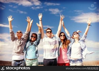 summer holidays and teenage concept - group of smiling teenagers in sunglasses holding hands up outside