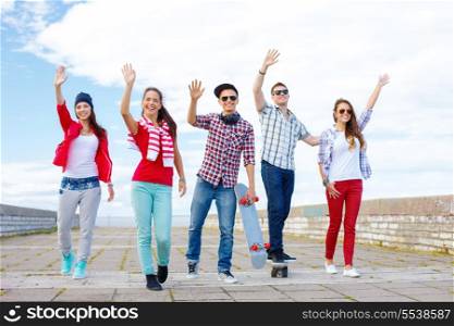 summer holidays and teenage concept - group of smiling teenagers waving hands outside
