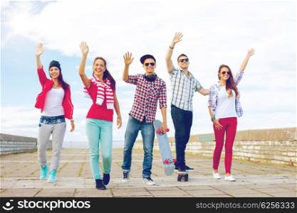 summer holidays and teenage concept - group of smiling teenagers waving hands outside. group of smiling teenagers waving hands