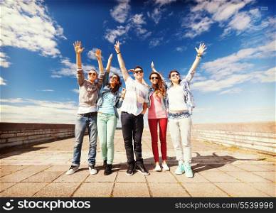 summer holidays and teenage concept - group of teenagers holding hands up outside