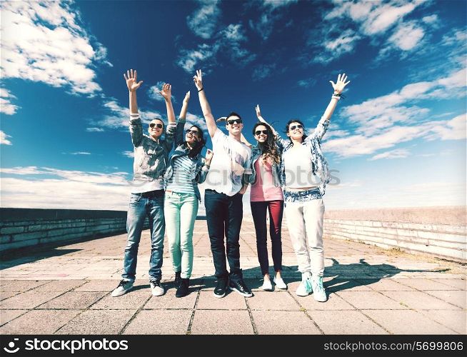 summer holidays and teenage concept - group of teenagers holding hands up outside