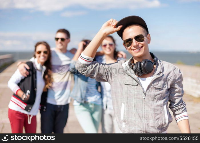 summer holidays and teenage concept - teenage boy in sunglasses, cap and headphones hanging out with friends outside