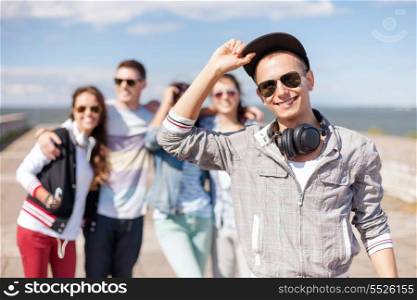 summer holidays and teenage concept - teenage boy in sunglasses, cap and headphones hanging out with friends outside