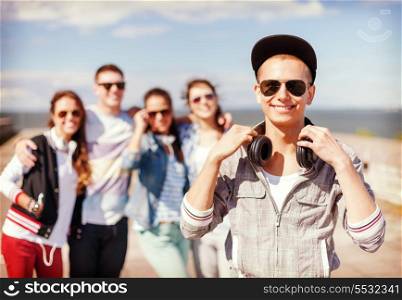 summer holidays and teenage concept - teenage boy in sunglasses, cap and headphones hanging out with friends outside
