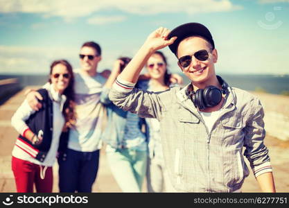 summer holidays and teenage concept - teenage boy in sunglasses, cap and headphones hanging out with friends outside