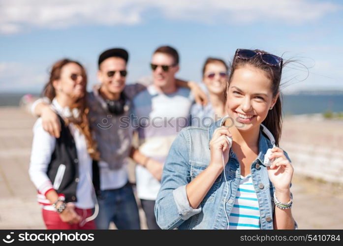 summer holidays and teenage concept - teenage girl in sunglasses and headphones hanging out with friends outside