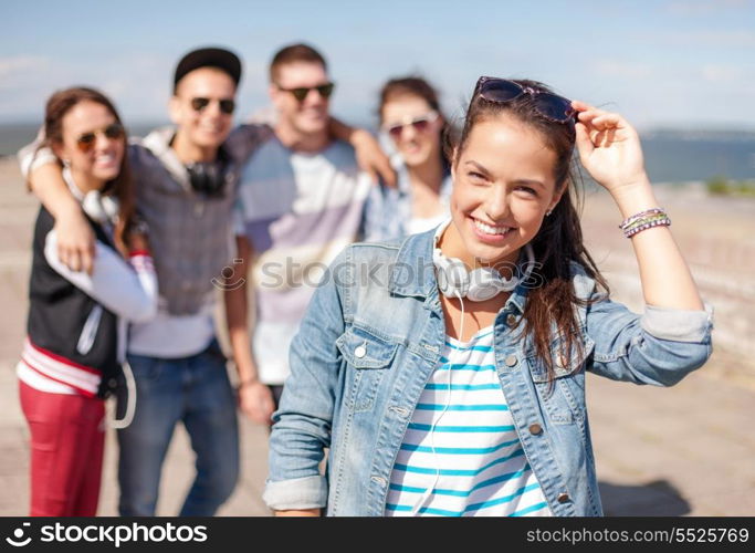 summer holidays and teenage concept - teenage girl in sunglasses and headphones hanging out with friends outside