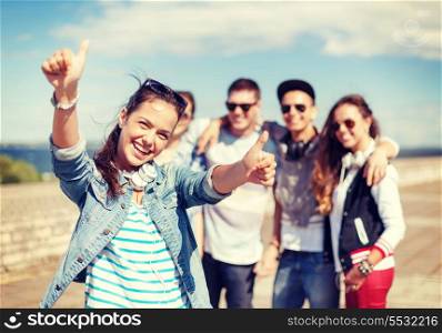 summer holidays and teenage concept - teenage girl in sunglasses and headphones hanging out with friends outside and showing thumbs up