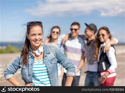 summer holidays and teenage concept - teenage girl in sunglasses and headphones hanging out with friends outside. teenage girl with headphones and friends outside