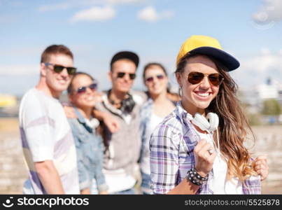 summer holidays and teenage concept - teenage girl in sunglasses, cap and headphones hanging out with friends outside