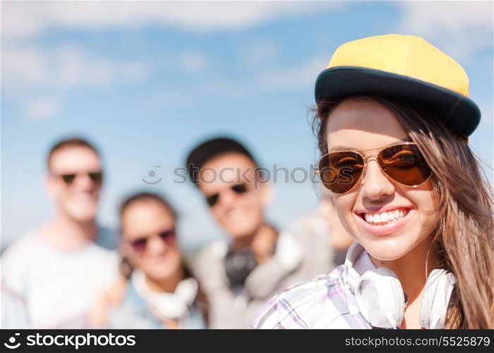 summer holidays and teenage concept - teenage girl in sunglasses, cap and headphones hanging out with friends outside