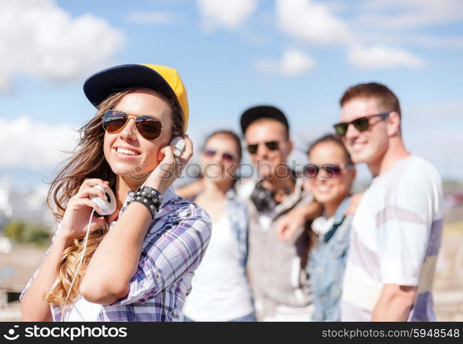 summer holidays and teenage concept - teenage girl in sunglasses, cap and headphones hanging out with friends outside