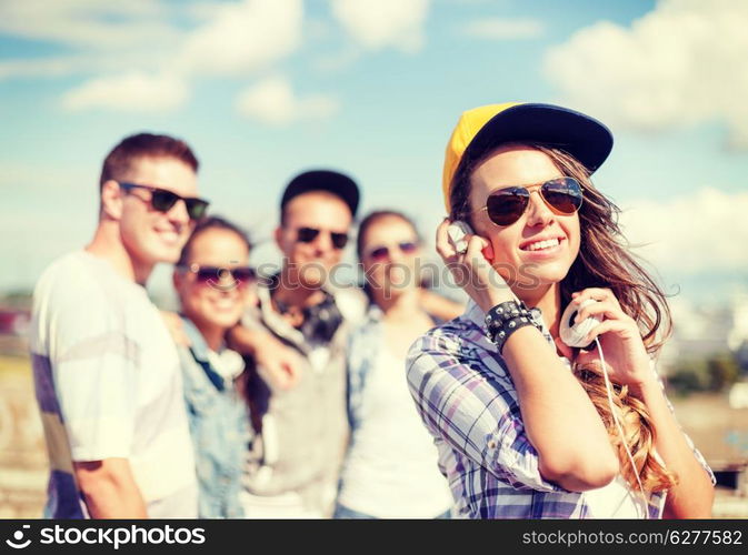 summer holidays and teenage concept - teenage girl in sunglasses, cap and headphones hanging out with friends outside