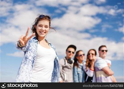 summer holidays and teenage concept - teenage girl in sunglasses hanging out with friends outside and showing thumbs up