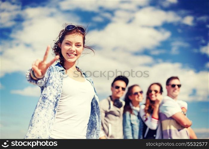 summer holidays and teenage concept - teenage girl in sunglasses hanging out with friends outside and showing thumbs up