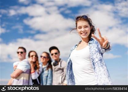 summer holidays and teenage concept - teenage girl in sunglasses hanging out with friends outside and showing thumbs up. teenage girl with headphones and friends outside