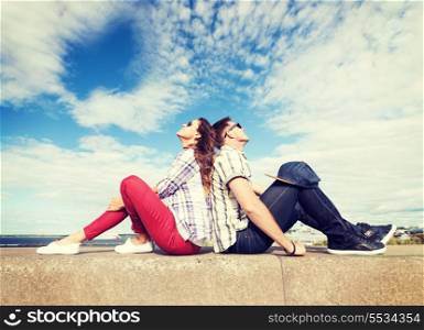 summer holidays and teenage concept - teenagers sitting back to back and looking up in the sky